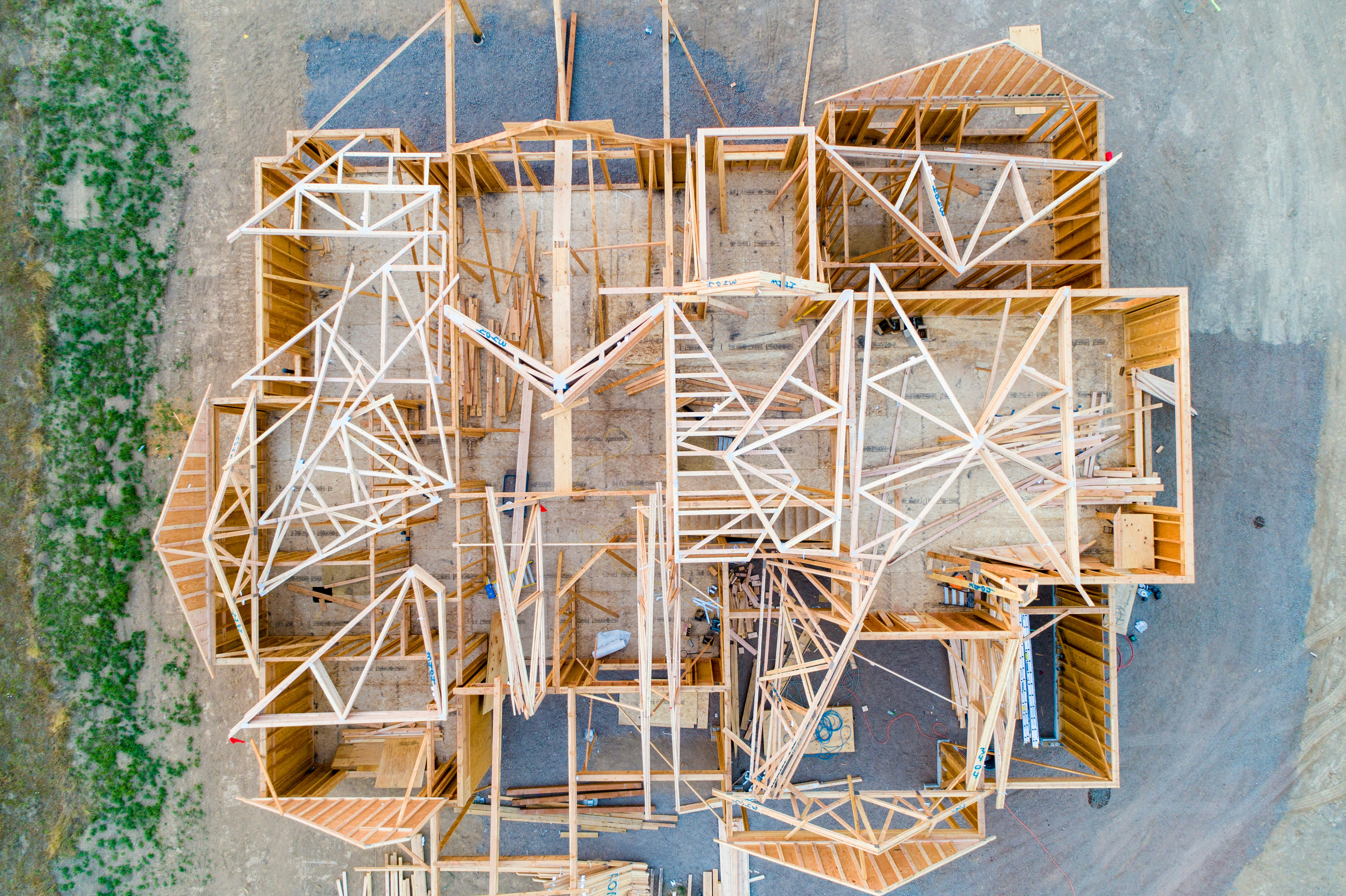 Aerial view of a house under construction with wooden framework and beams forming the structure. The setting suggests progress and development.